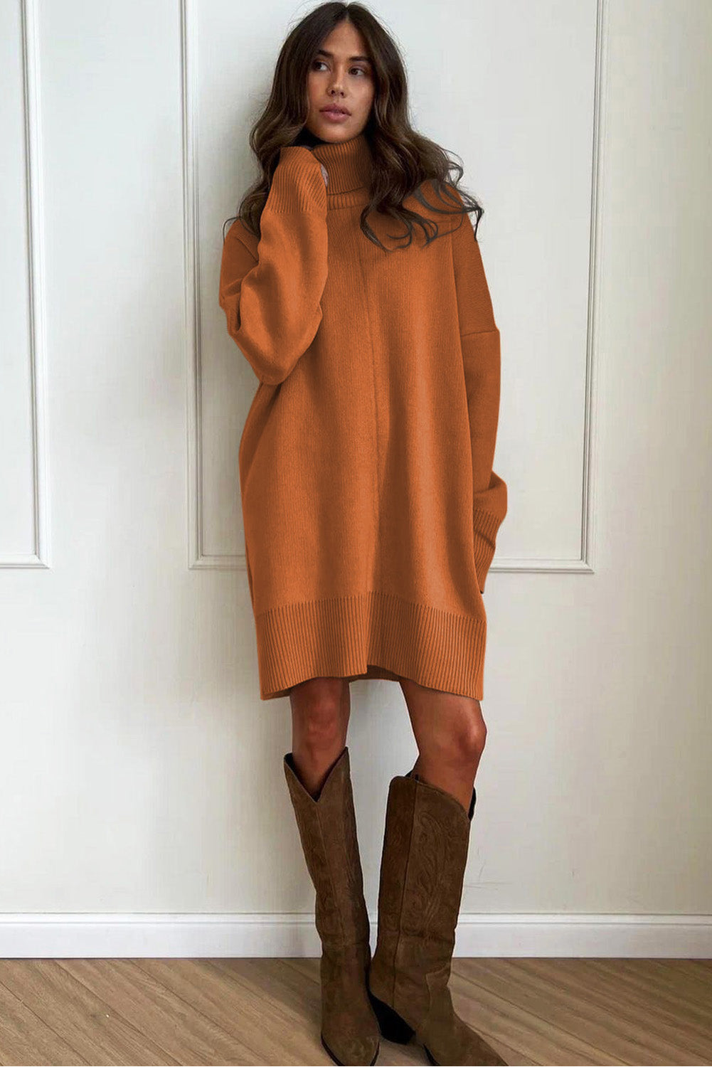 Woman wearing a brown Oversized Turtleneck Jumper Dress and boots against a white wall.