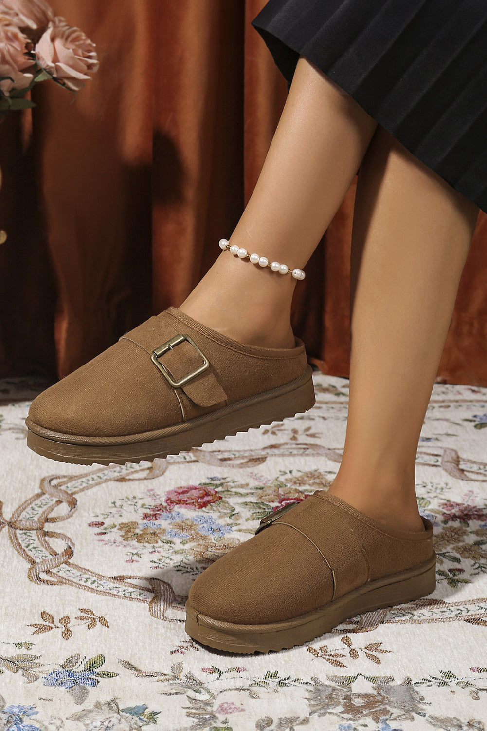 Brown vegan suede clog slippers with a buckle on a floral rug