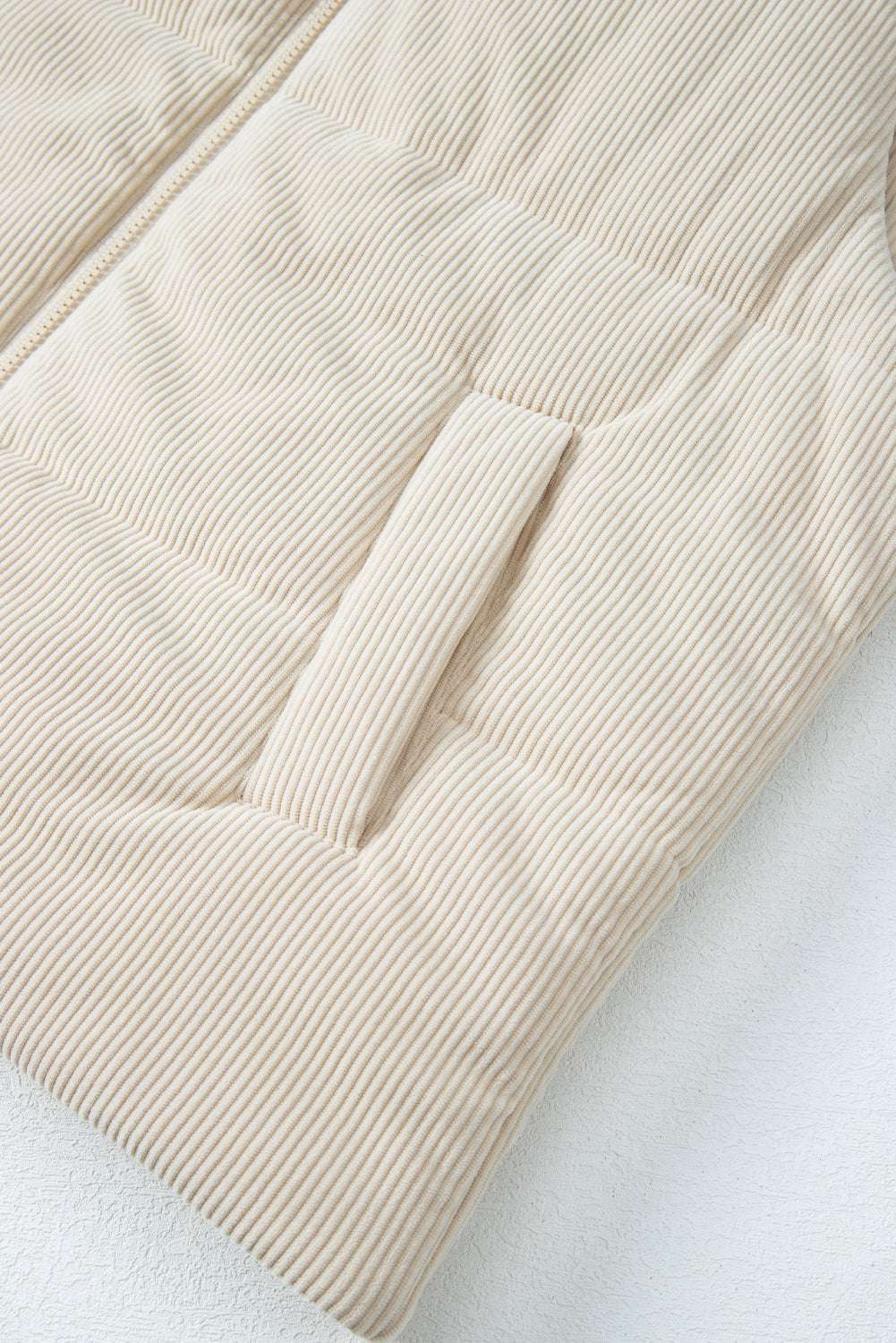 Detail of front pocket on beige corduroy puffer gilet, showing soft ribbed fabric and quilted construction for winter comfort.