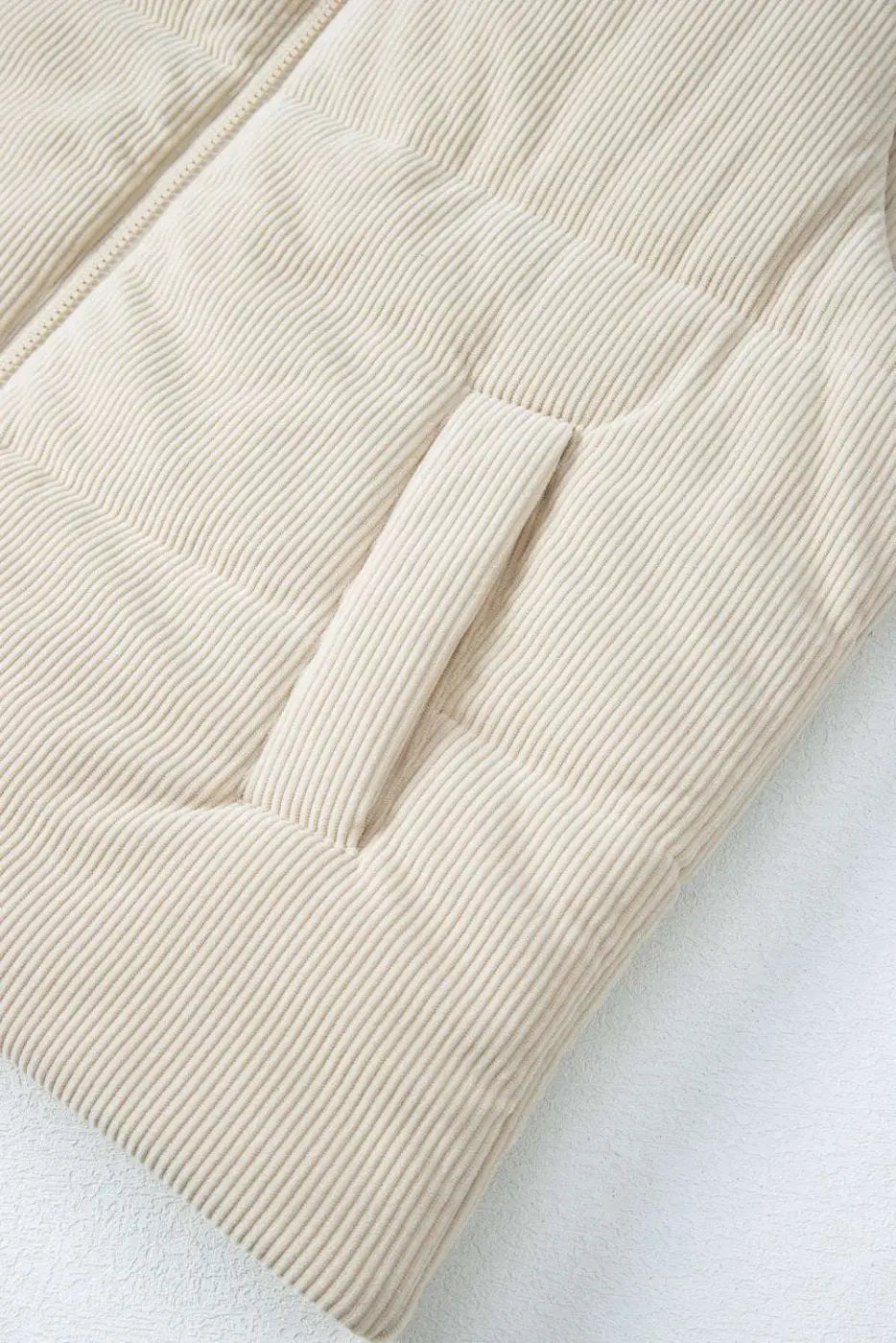Detail of front pocket on beige corduroy puffer gilet, showing soft ribbed fabric and quilted construction for winter comfort.