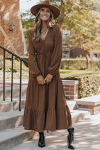 Full front view of Brown Long Sleeve Tiered Maxi Dress with modern A-line cut and cinched waist, styled with a wide-brim hat.