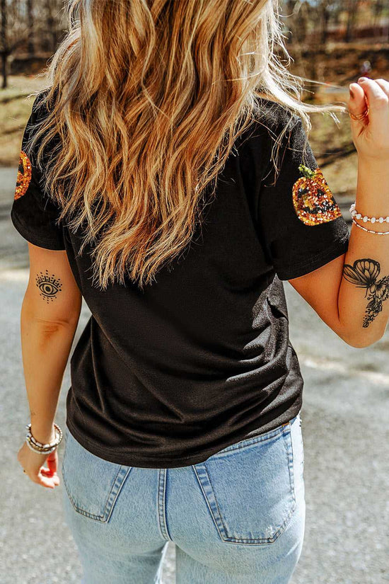 Person wearing a black t-shirt with pumpkin designs on the sleeves, standing outdoors.