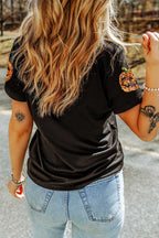 Person wearing a black t-shirt with pumpkin designs on the sleeves, standing outdoors.