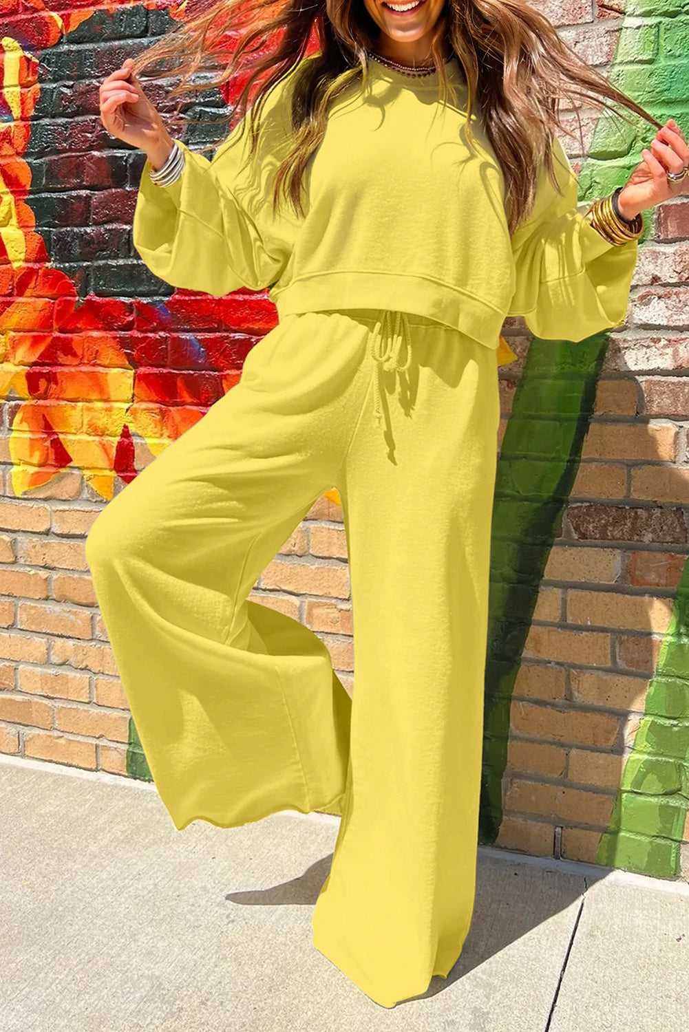 Yellow Drop Crop Wide-Leg Pants Set styled with playful pose against floral mural, showcasing vibrant fall loungewear fashion.