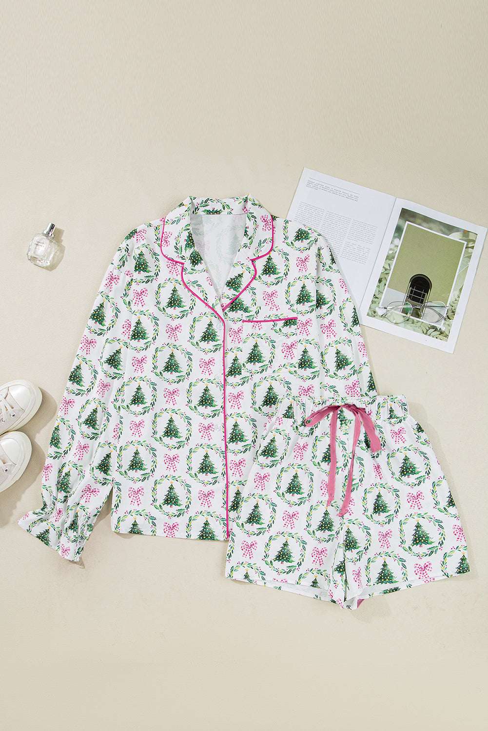 Flat lay of Ladies White Christmas Print Velvet Trim Pyjamas with green tree and pink bow print, pink piping and drawstring shorts.