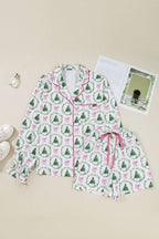 Flat lay of Ladies White Christmas Print Velvet Trim Pyjamas with green tree and pink bow print, pink piping and drawstring shorts.