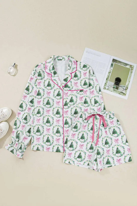 Flat lay of Ladies White Christmas Print Velvet Trim Pyjamas with green tree and pink bow print, pink piping and drawstring shorts.