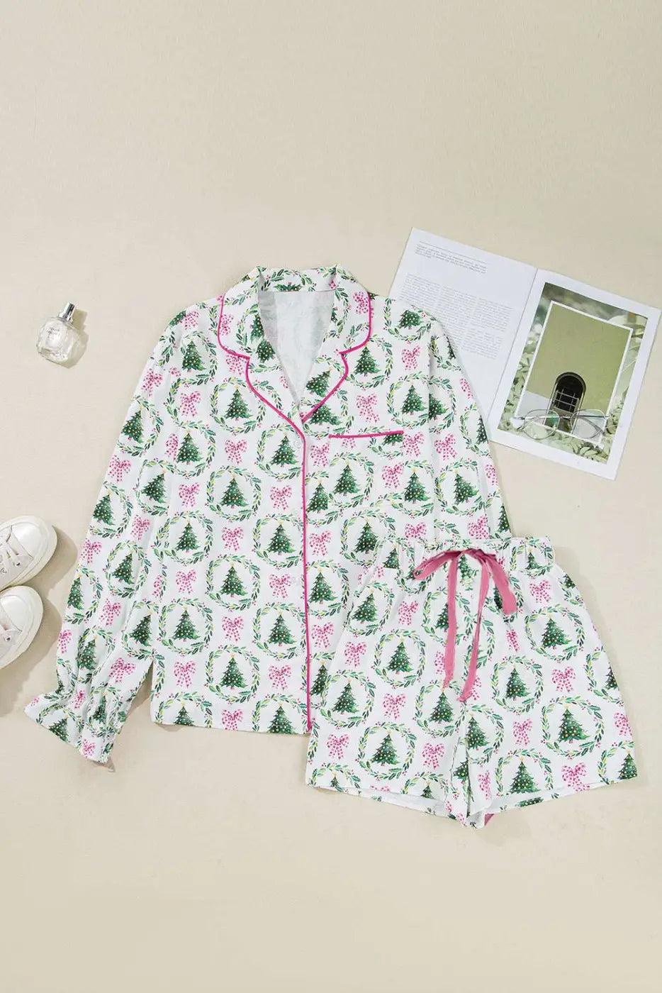 Flat lay of Ladies White Christmas Print Velvet Trim Pyjamas with green tree and pink bow print, pink piping and drawstring shorts.