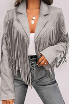 Close-up of gray cropped fringe faux suede jacket with lapel collar and tassel detailing, styled with gray denim and layered gold jewelry.