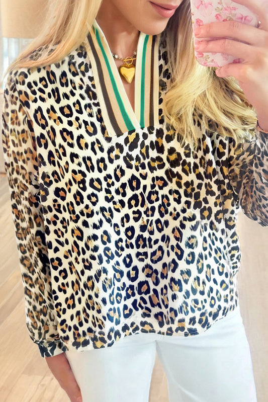 Person wearing a leopard print top with a striped collar, holding a pink cup.