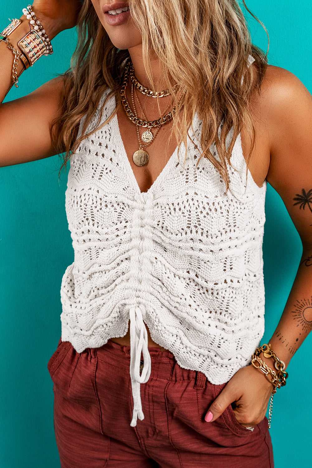 White crochet tank top with ruched drawstring front, styled for summer with casual red shorts and gold accessories.