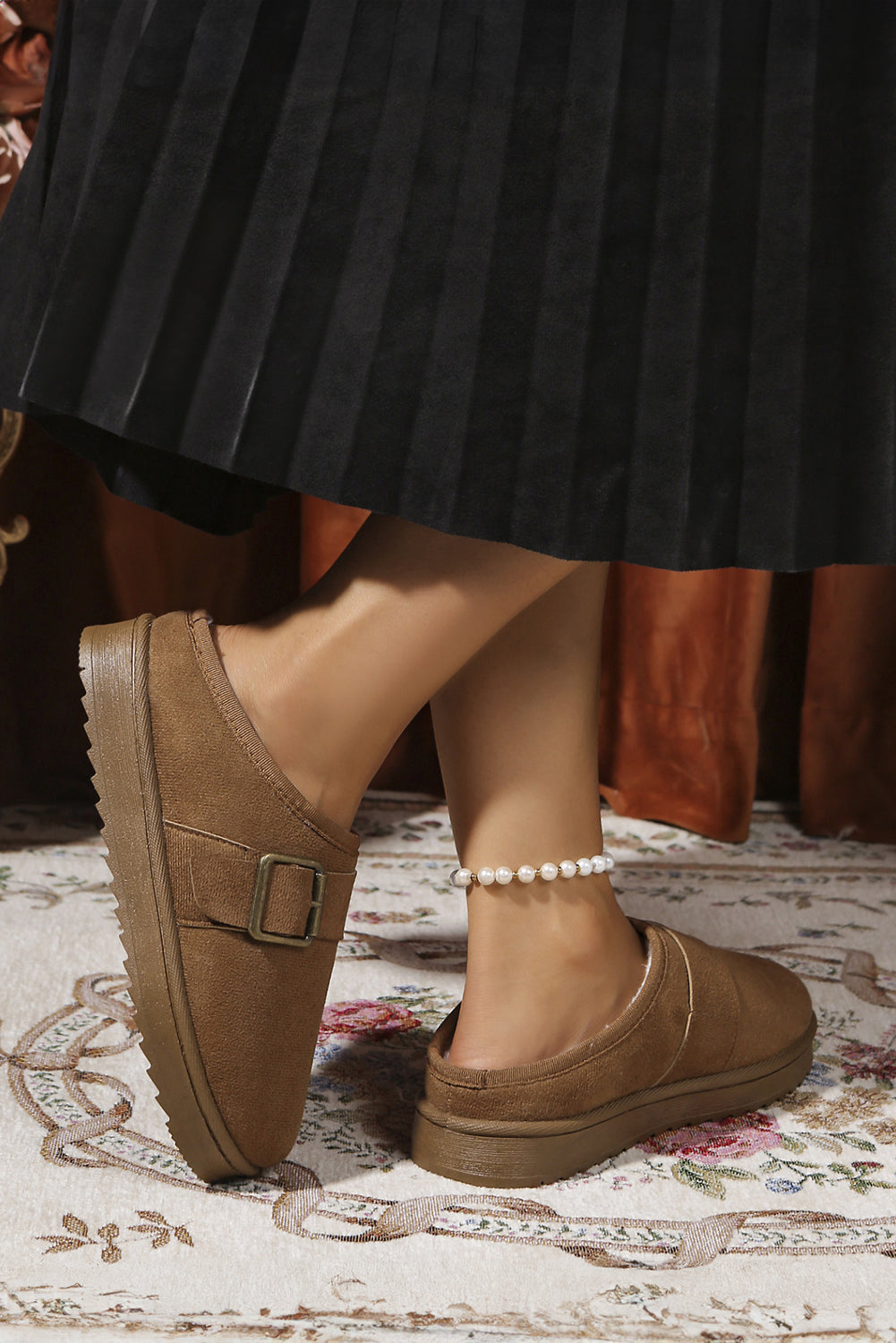 Brown vegan suede clog slippers worn with a black skirt on a patterned rug.