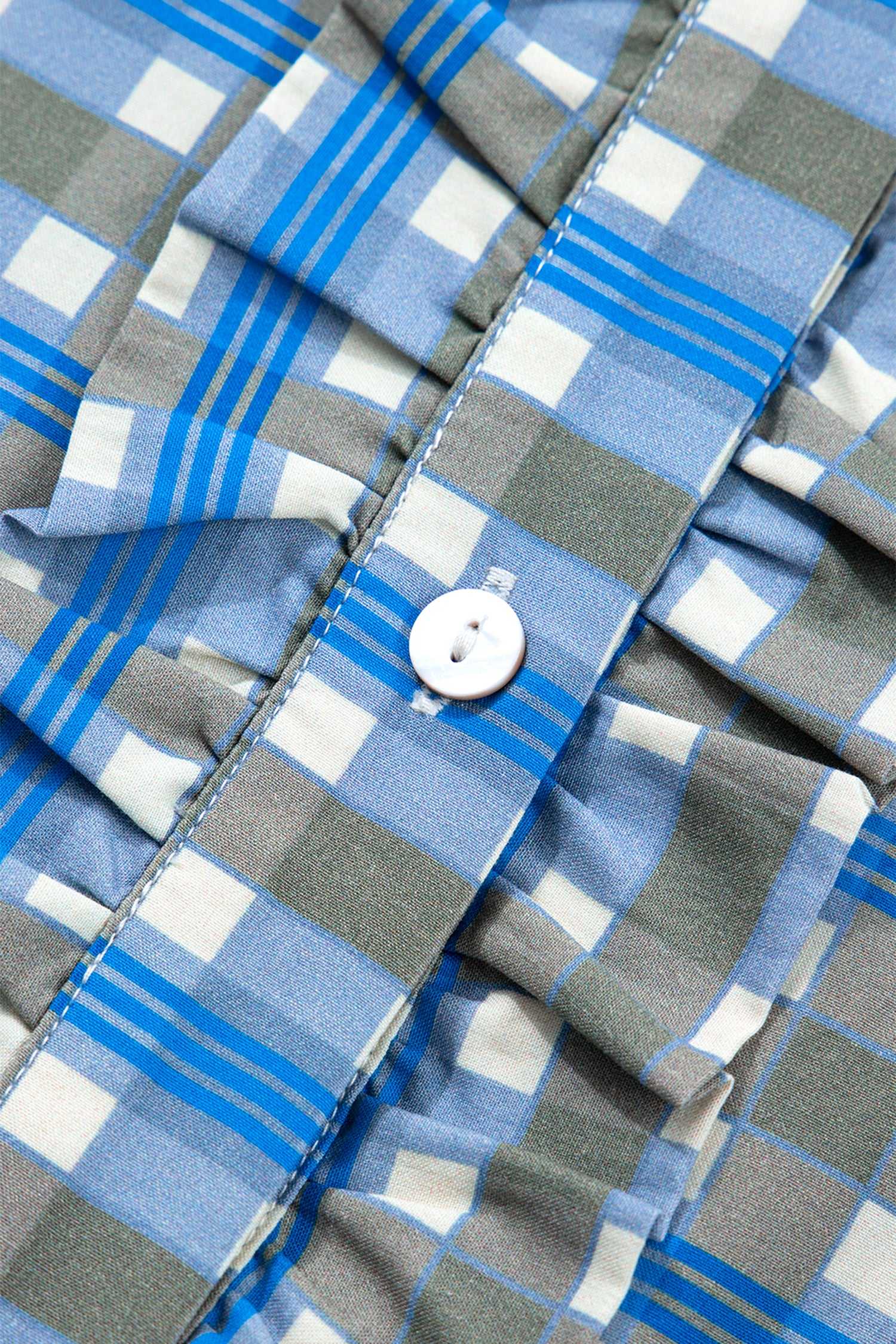 Close-up of frilled front and white button on blue plaid cotton blouse, showcasing half-button design and soft fabric texture.
