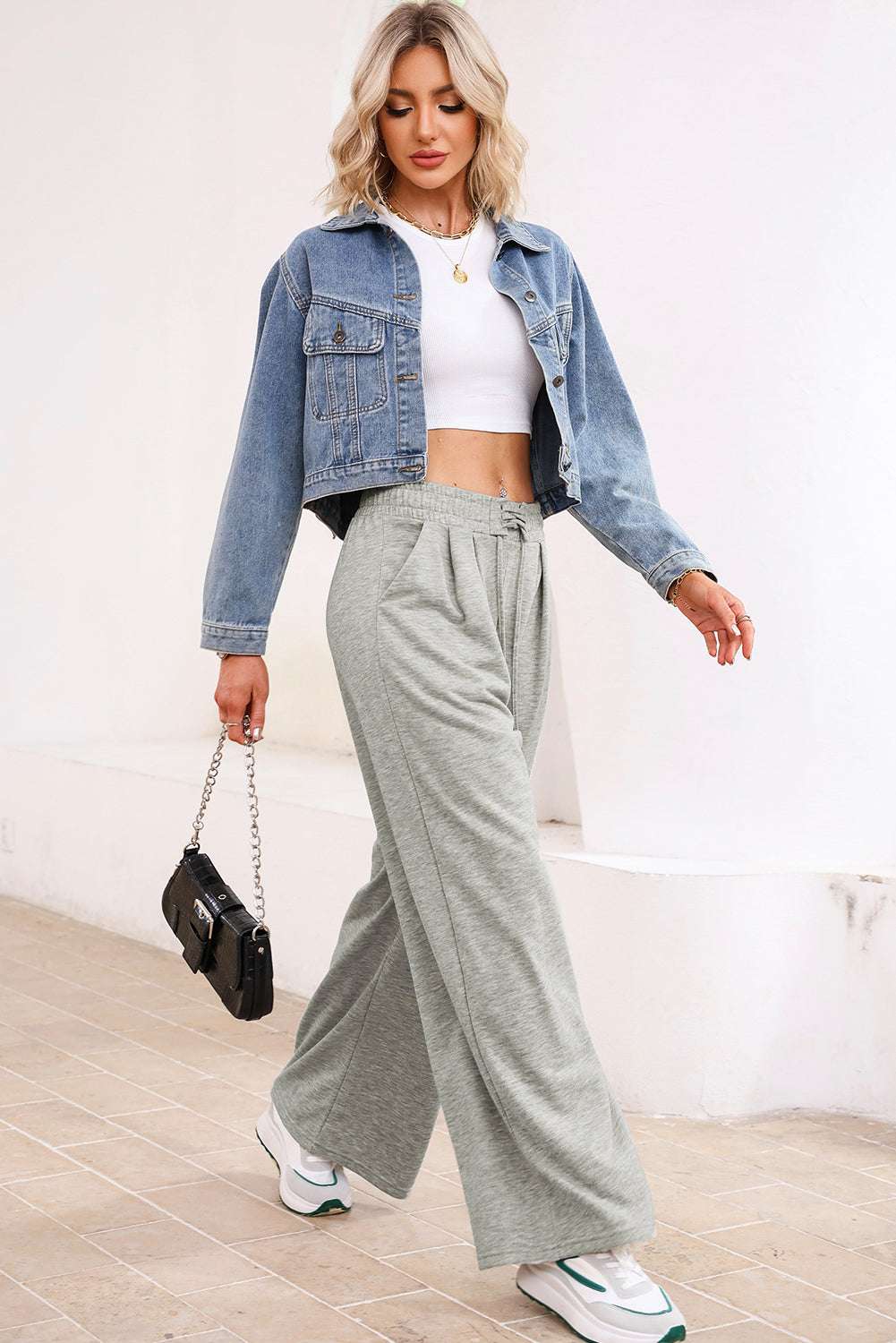 Model wearing gray pleated sweatpants with a white crop top and denim jacket, showcasing a trendy casual outfit.