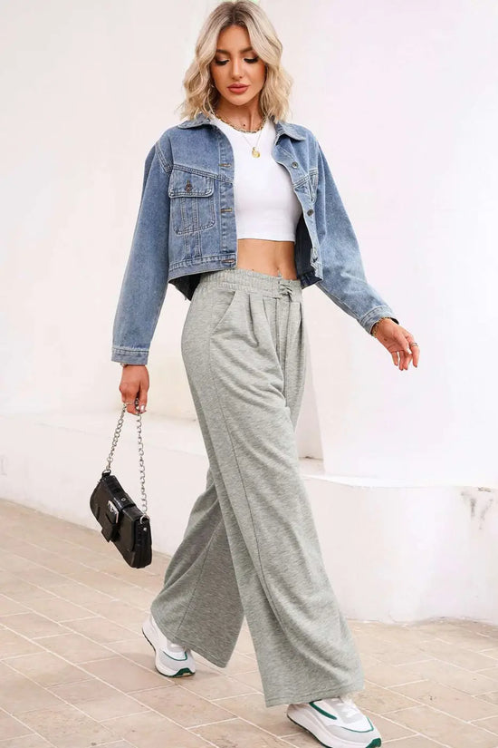 Model wearing gray pleated sweatpants with a white crop top and denim jacket, showcasing a trendy casual outfit.