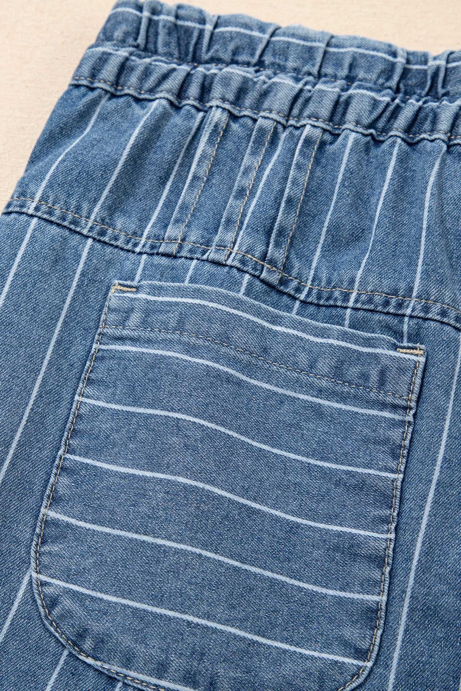 Detail of back pocket and elastic waistband on pinstripe denim trousers, highlighting the casual and functional design.