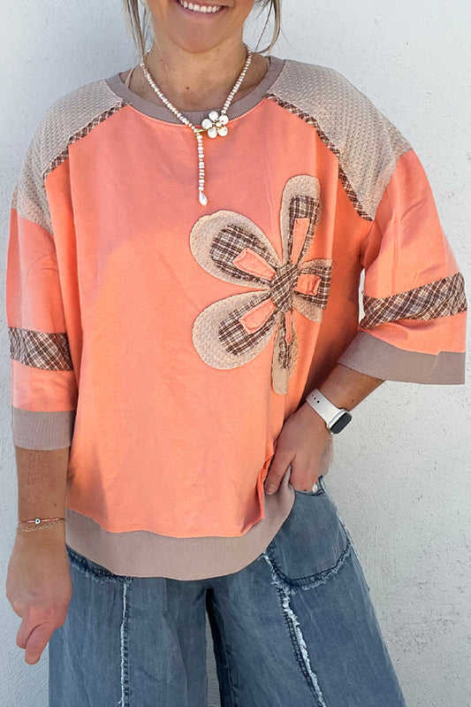 Person wearing a peach-colored top with a floral design and denim pants against a white background