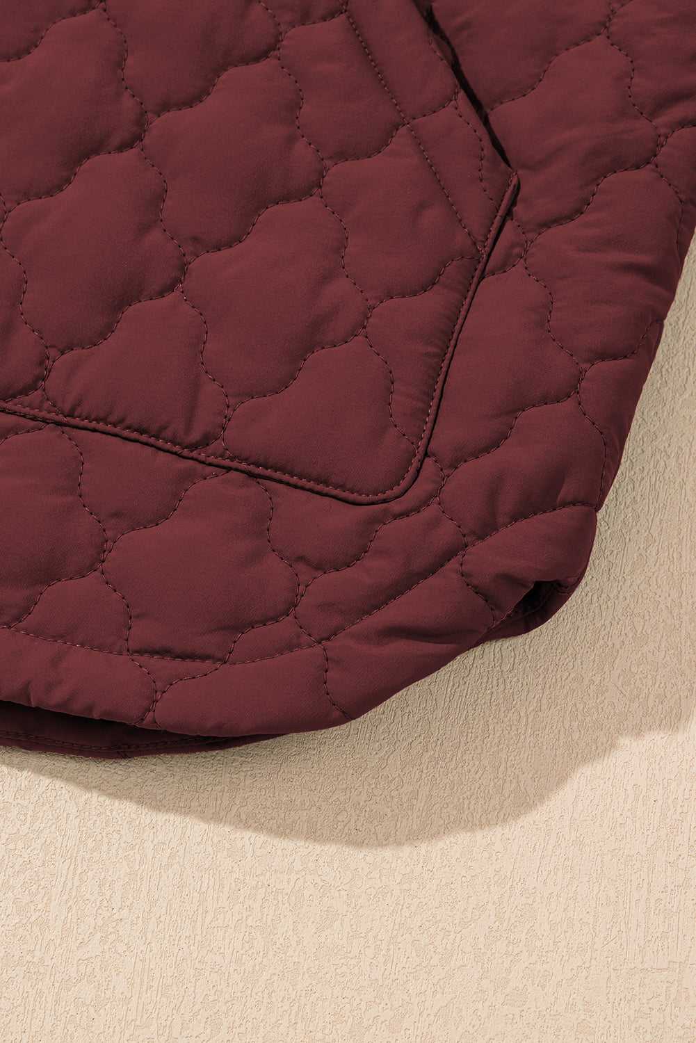 Close-up of hem detail on burgundy Flower‑Quilted Winter Gilet showing curved edge and floral quilt stitching for stylish winter outerwear.
