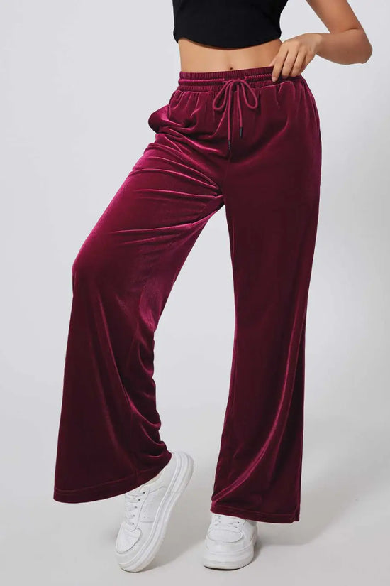Side angle of burgundy velvet yoga pants showing plush texture and flowy wide-leg design, styled with white sneakers for comfort.