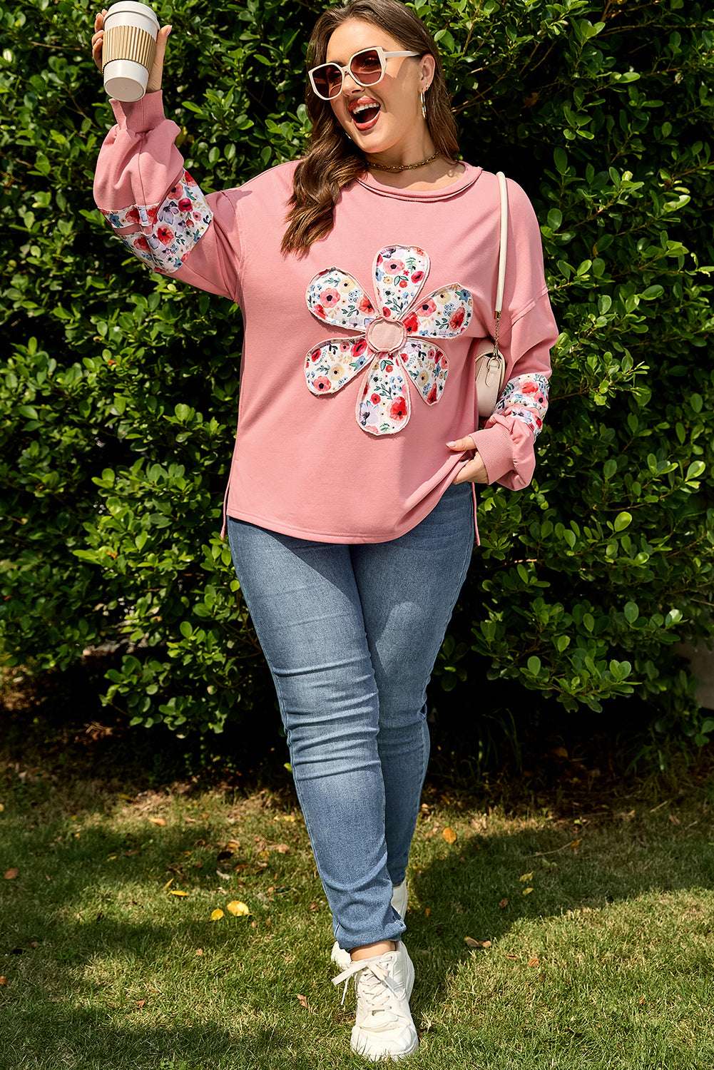 Full body shot of woman wearing Curve Blush Peach Floral Appliqué Sweatshirt for Women with jeans and sneakers, showcasing casual plus size outfit.