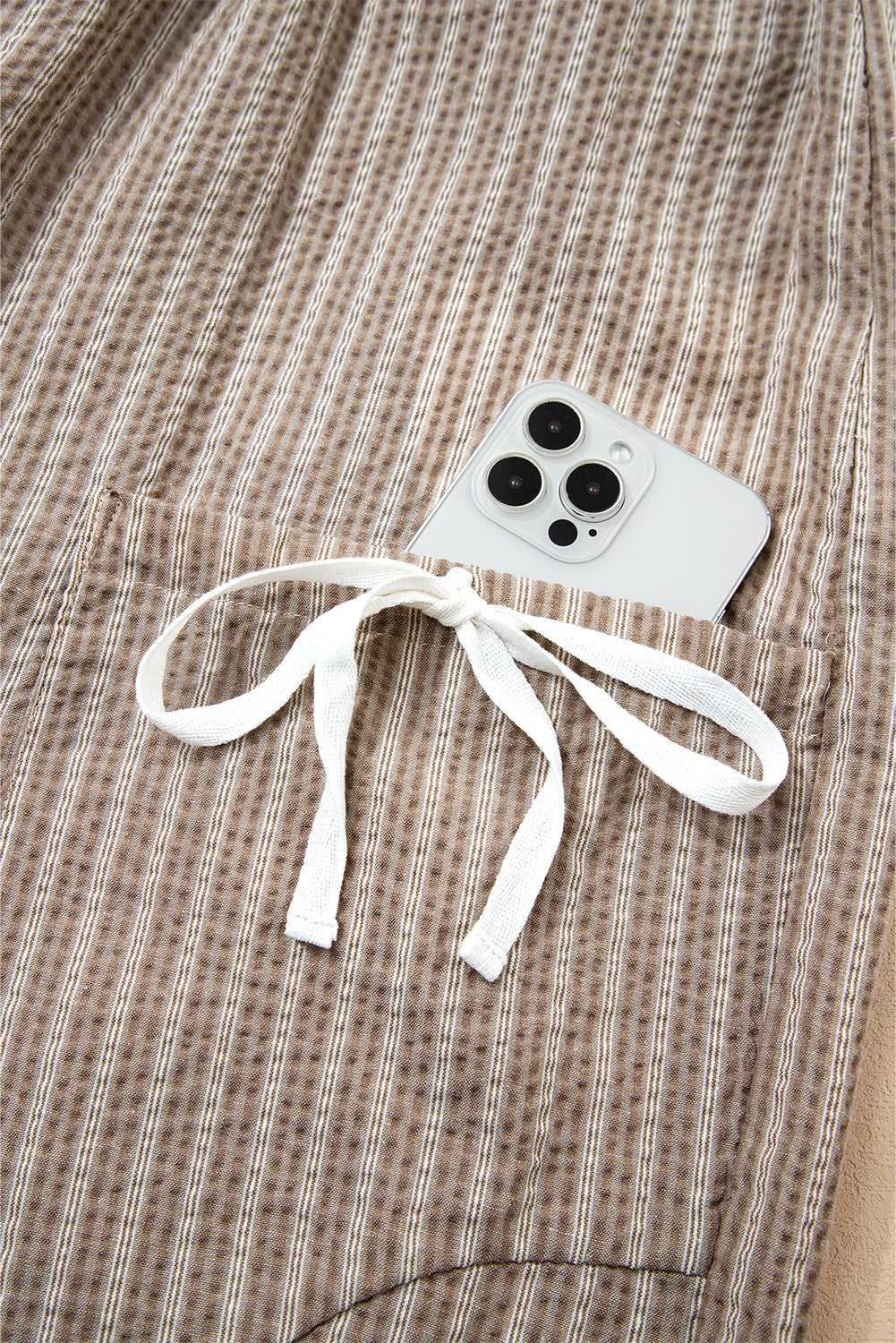 Detail of side cargo pocket on Brown Stripe Joggers with white bow tie and smartphone inside.