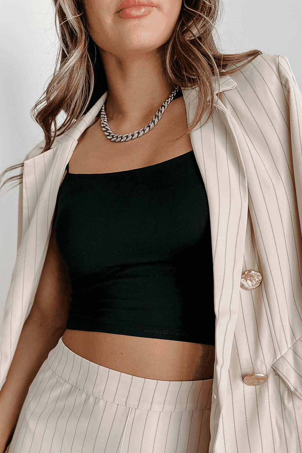Black skinny fit crop top layered under a beige pinstripe blazer, ideal for casual chic or night-out looks.