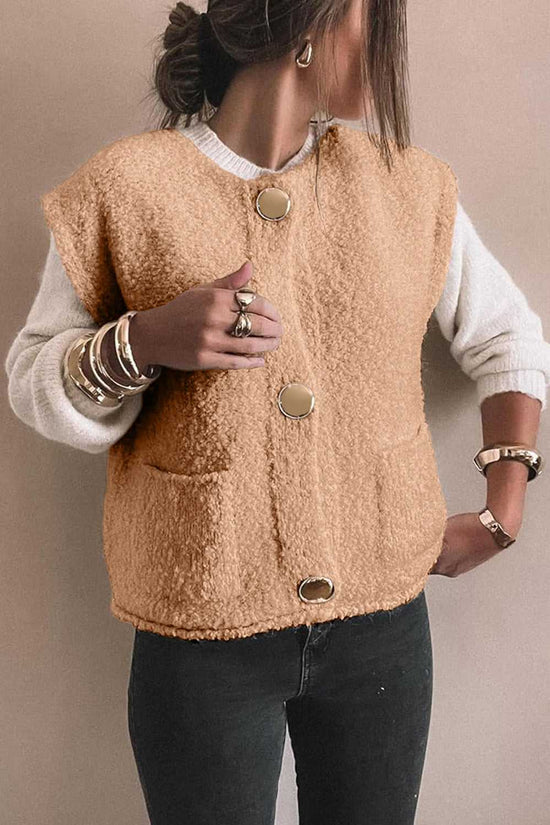 Beige fuzzy vest with oversized buttons and front pockets, styled with white knit sleeves and stacked bangles for a modern winter look.