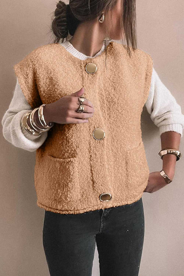 Beige fuzzy vest with oversized buttons and front pockets, styled with white knit sleeves and stacked bangles for a modern winter look.