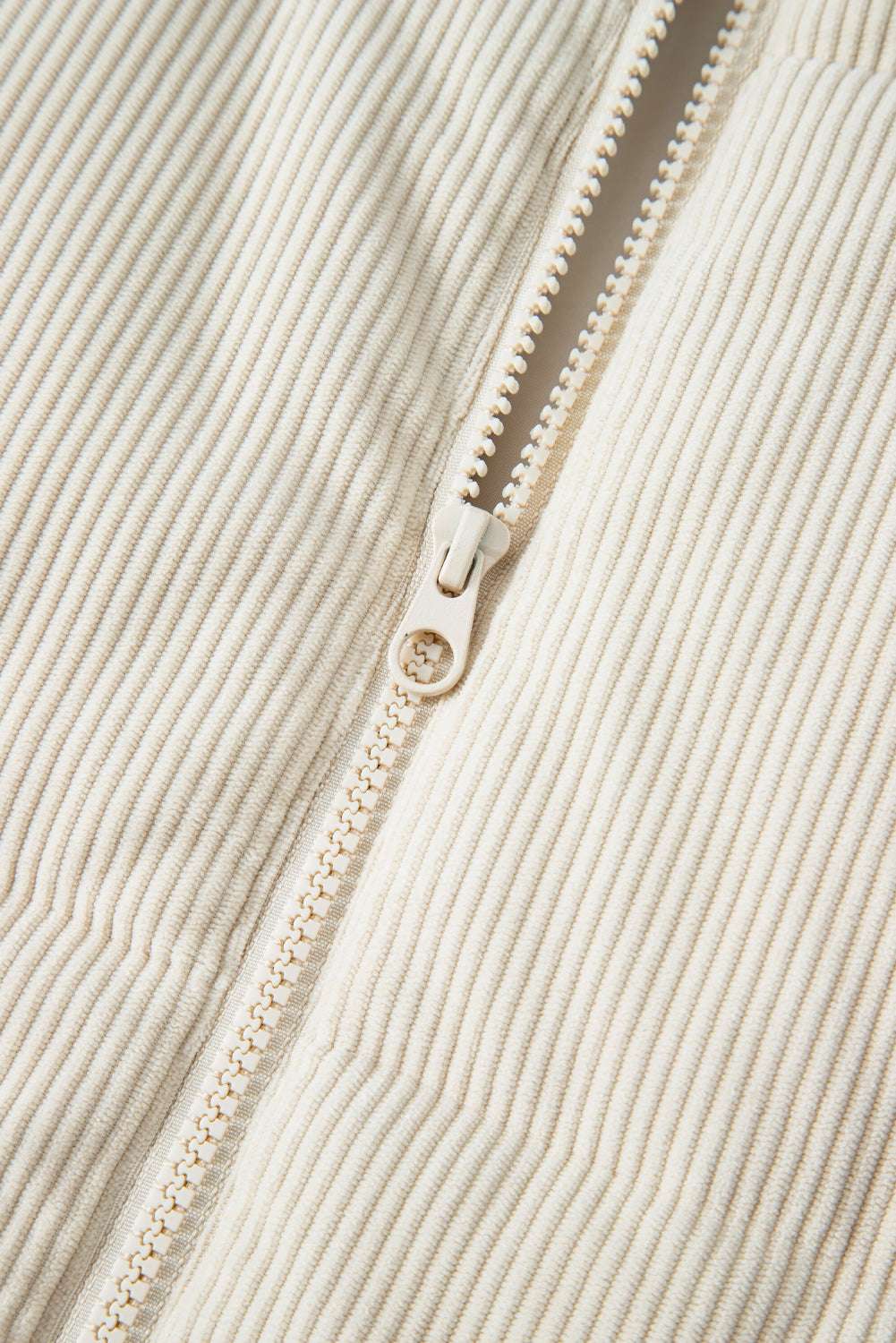 Close-up of zipper on beige corduroy puffer gilet, showcasing durable hardware and fine ribbed corduroy texture.