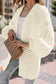 Close-up of cozy white oversized cardigan with textured chunky knit and balloon sleeves, styled with casual accessories.