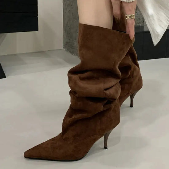 Slouchy brown suede knee-high boots with kitten heel and pointed toe, offering a relaxed yet fashionable silhouette.