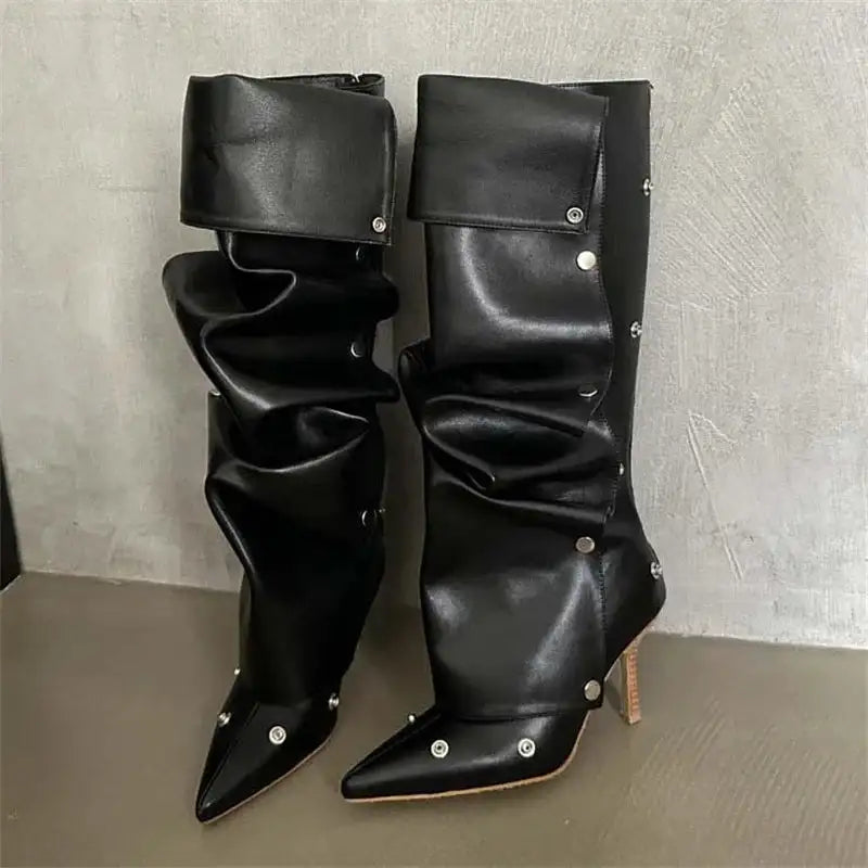 Black faux leather knee high boots for women with pleated folds and thin heels, accented with silver buttons for edgy appeal.