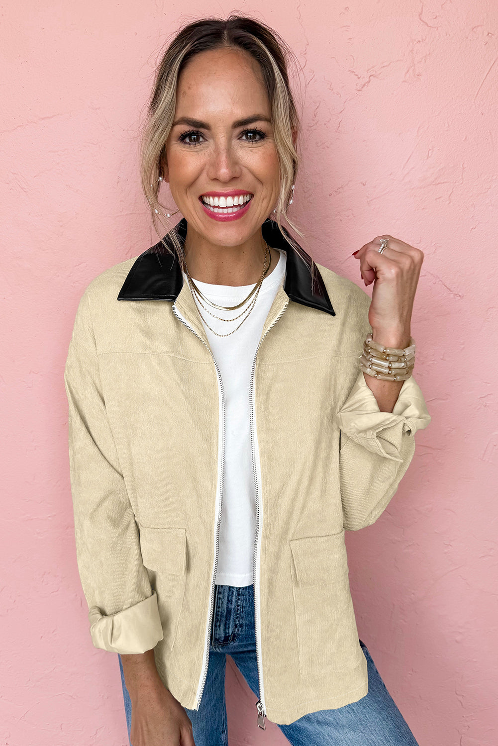 Woman wearing a beige jacket with a black collar against a pink background