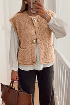 Cozy fleece gilet in beige with fuzzy texture, large button accents, and front pockets, styled over a white blouse and black jeans.