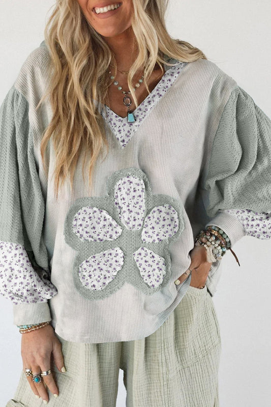 Woman wearing a light gray sweater with floral patterns on a white background