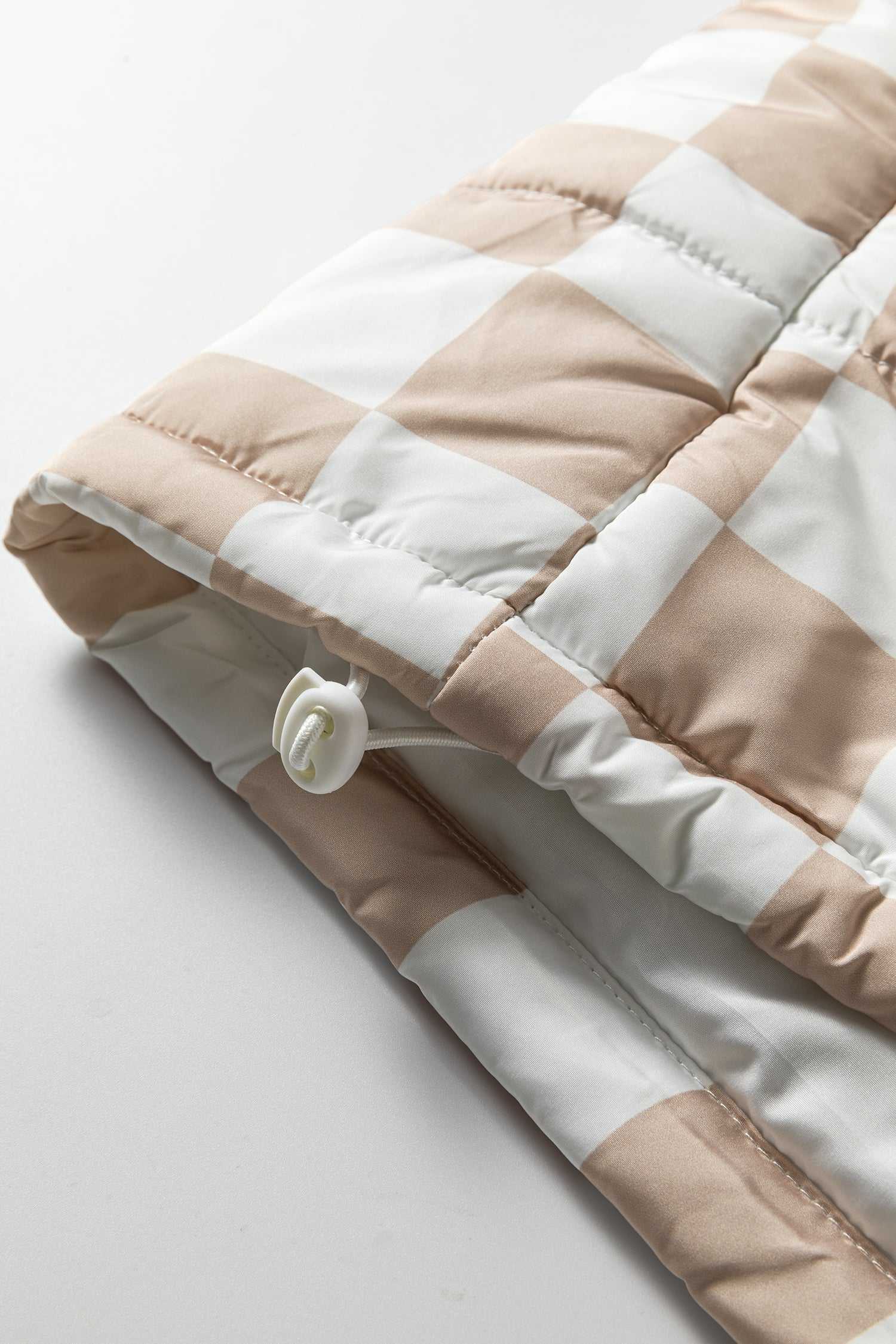 Close-up of adjustable drawcord hem on khaki plaid quilted gilet, designed for a snug fit and added warmth in winter.