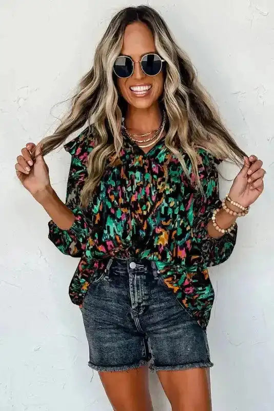 Smiling model in black Abstract Ruffle Blouse with Puff Sleeves and sunglasses, styled with black denim shorts.