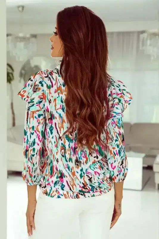 Back view of Abstract Ruffle Blouse with Puff Sleeves paired with white pants, highlighting the ruffle shoulder design.