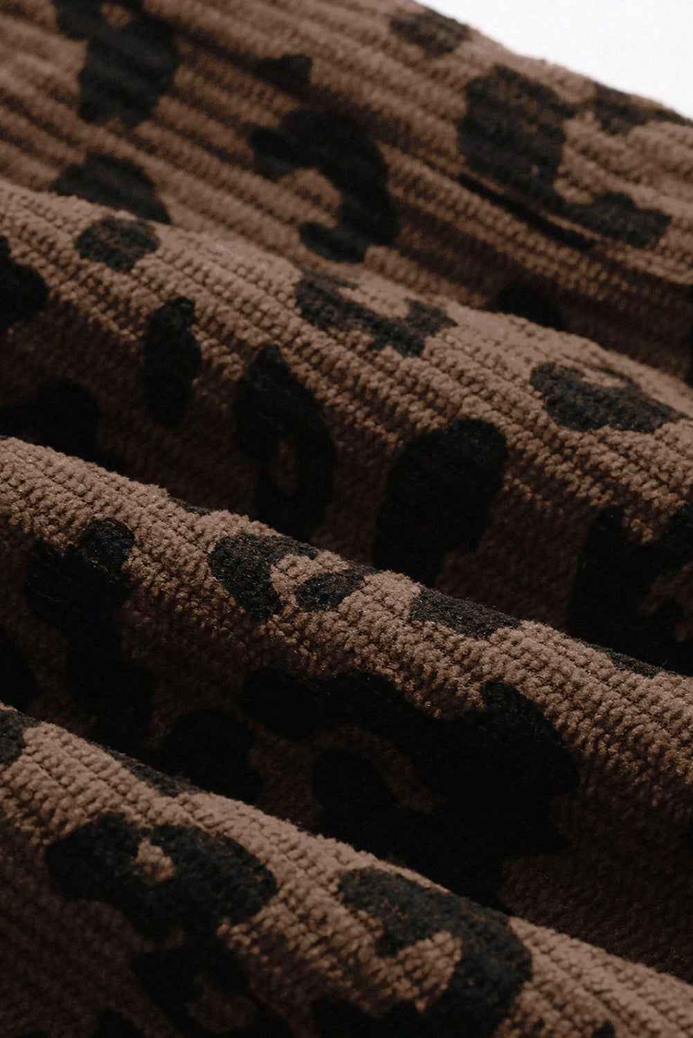 Close-up of soft brown corduroy fabric with black leopard print, highlighting texture and quality of trendy fall trousers.