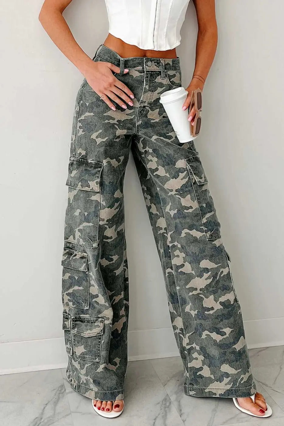 Front view of camo cargo jeans women styled with a white top. Wide leg denim pants with utility pockets and high waist in green camo print.