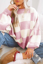 Person wearing a pink and white checkered sweater and blue jeans, sitting on a white surface.