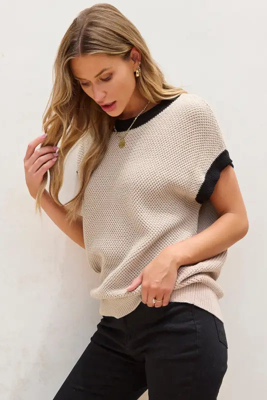 Blonde woman in light french beige knit sweater with black trim, batwing sleeve style