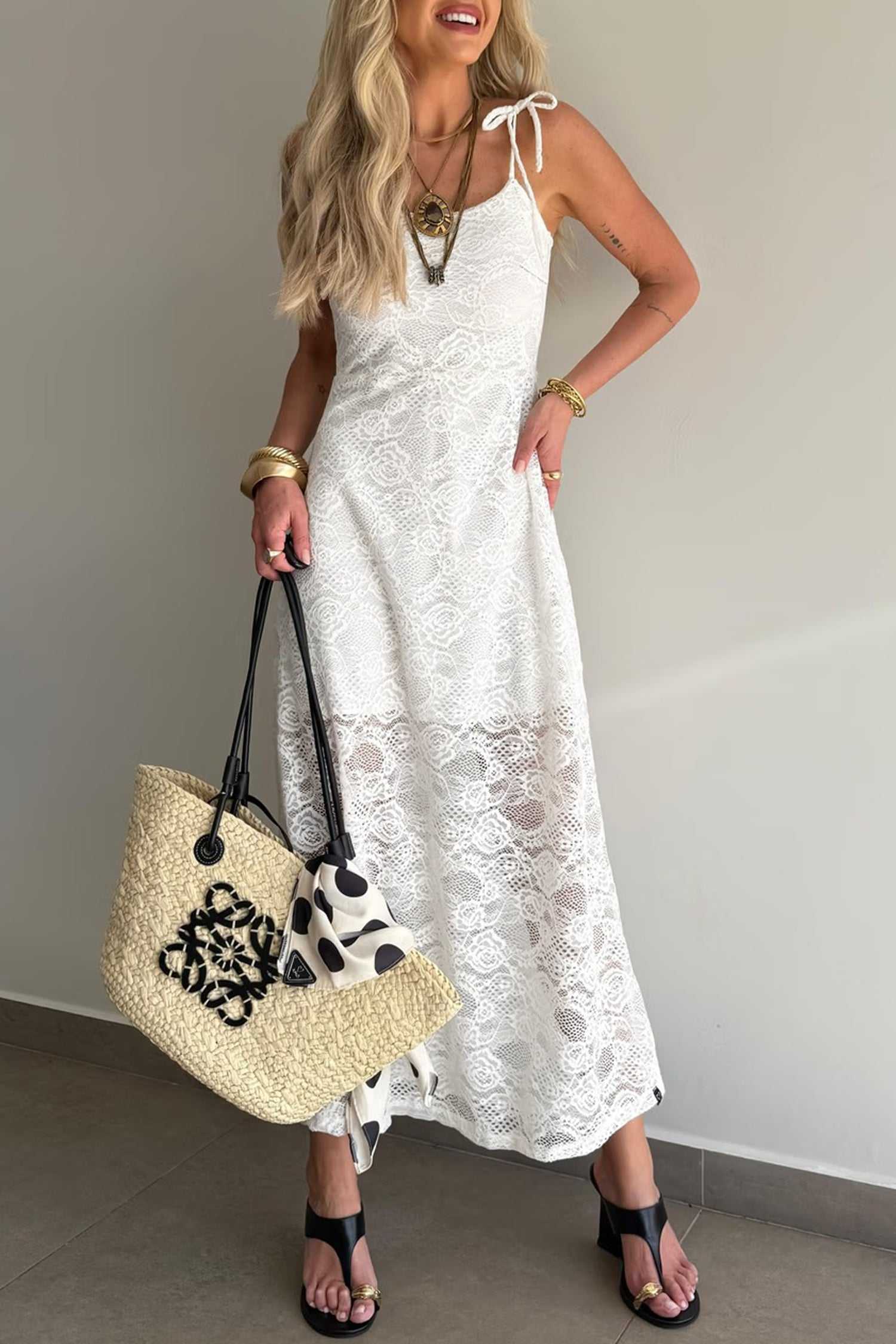 White Lace Overlay Maxi Dress with spaghetti straps and tie-back detail, styled with black heels and straw tote for summer occasions.