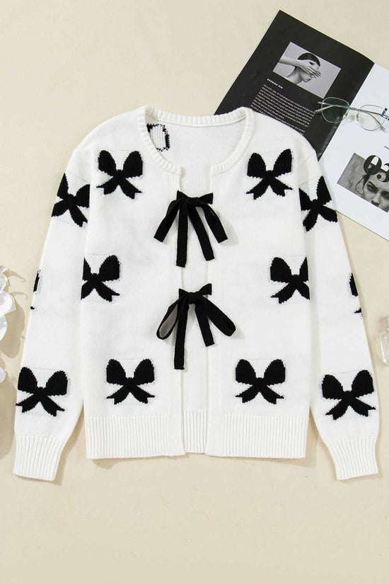 Flat lay of White Bow‑Lace Knit Cardigan with black bow patterns and ribbon ties, highlighting its soft knit texture and elegant design.
