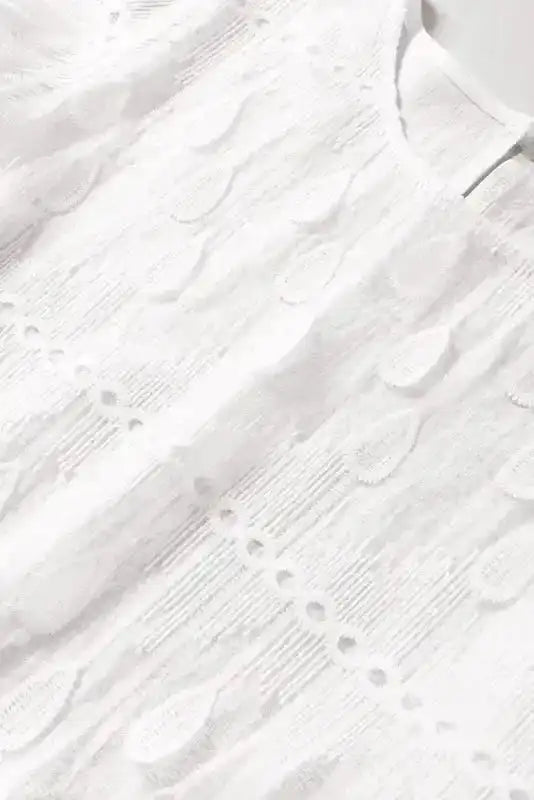 Detailed view of embroidered mesh fabric on beige blouse. Showcases vertical stitching and teardrop lace accents for texture.