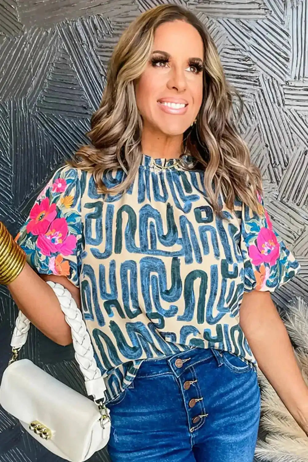 Smiling woman wearing a multi-colour embroidered top with puff sleeves and frilled neck, paired with denim jeans and white handbag.
