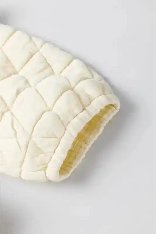Close-up of cream quilted sleeve with elastic cuff from modern loungewear set, highlighting cozy fabric texture.