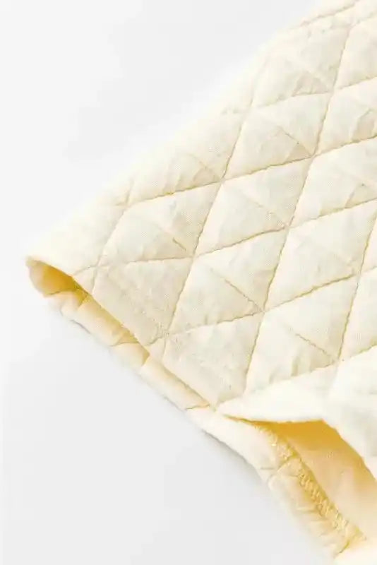 Detail of cream quilted shorts fabric from trendy loungewear set, showcasing diamond stitching and soft material.