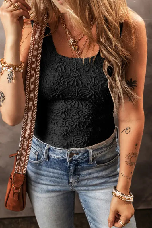 Woman in black floral jacquard tank top with jeans, jewelry, and tattoos, relaxed style