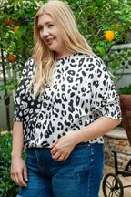 Smiling model wearing black and white leopard print plus size blouse with smocked sleeves, perfect for summer outings.